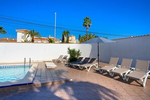 Un área junto a la piscina con sillones de descanso, piscina y cielo azul despejado.