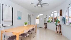 A spacious dining area with a long wooden table and chairs, a ceiling fan, and a view through an arched window.