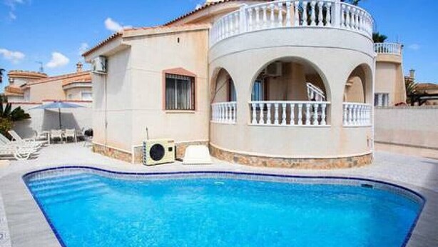 A swimming pool with a white building featuring arched windows and balconies.