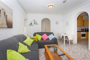 A living room with a grey sofa, colorful cushions, a coffee table, and a kitchen visible through an archway. - CH Villa Rubira Ciudad Quesada (Ciudad Quesada)