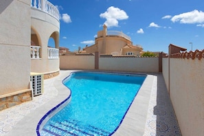 A swimming pool with a curved edge, a white wall with a decorative pattern, and a clear blue sky.