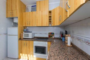 A compact kitchen with wooden cabinets, a built-in oven, a microwave, and a granite countertop.
