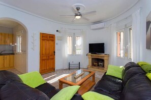 Ein Wohnzimmer mit einer Couch, einem Fernseher, einem Kamin und einem Deckenventilator.