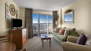 A hotel room with a television, a dining table, a sofa, and a balcony with a view. - Wonderful Oceanfront King Suite + Official On-Site Rental Privileges (Myrtle Beach)