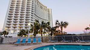 A high-rise hotel with multiple balconies, a swimming pool with lounge chairs, and palm trees. - Wonderful Oceanfront King Suite + Official On-Site Rental Privileges (Myrtle Beach)