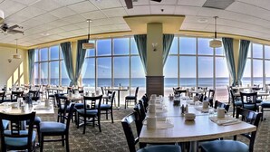 A large dining area with tables and chairs, large windows with curtains, and ceiling fans. - Wonderful Oceanfront King Suite + Official On-Site Rental Privileges (Myrtle Beach)