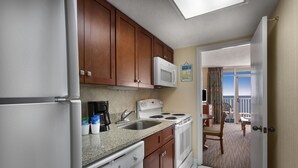 A compact kitchen with wooden cabinets, a microwave, a stove, and a dishwasher. - Wonderful Oceanfront King Suite + Official On-Site Rental Privileges (Myrtle Beach)
