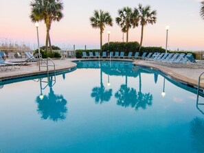 Une piscine entourée d’une clôture, avec des chaises longues et des palmiers.