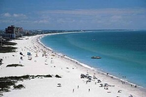 A beach with a sandy shore, a few buildings in the background, and a clear blue sky.