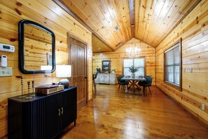 L’intérieur d’un chalet en bois comprend un coin repas, un meuble noir avec un miroir et, au fond, une cuisine.