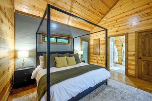 A four-poster bed with a headboard, a nightstand with a lamp, and a view of a bathroom through an open door.