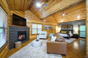 A log cabin interior with a fireplace, a sofa, a bed, and a painting on the wall.