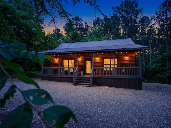 A wooden cabin with a porch, a front door, and a gravel driveway.