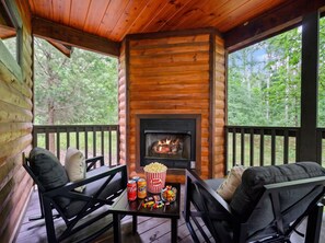 Una cabaña de troncos con chimenea, mobiliario exterior y una mesa con aperitivos.