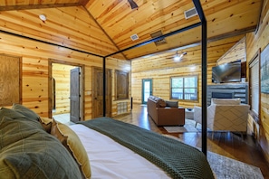Interior de una cabaña de troncos con cama, sofá, televisor y paredes de madera.