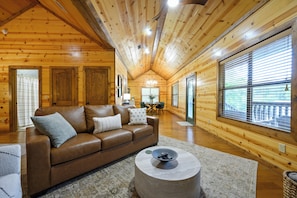 A cozy log cabin interior with a leather sofa, a round coffee table, and wooden walls.