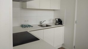 Una cocina compacta con armarios blancos, un lavamanos de acero inoxidable, un hervidor y un paño escocés sobre la encimera.