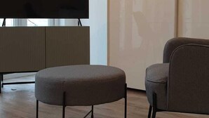 Una sala de estar moderna con un televisor de pantalla plana sobre un mueble bajo, un reposapiés gris y un sofá gris.