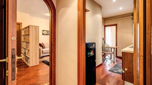 A hallway with a wooden door frame, a bookshelf, a white sofa, a dining area with a table and chairs, and a kitchen area with a refrigerator. - Beautiful apartment near San Pietro. Comfortable, silent, WI-FI, accessories. (Roma)