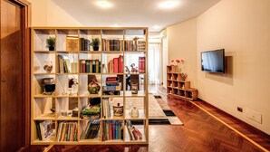 A spacious living room with a large wooden bookshelf filled with books and decorative items, a flat-screen TV mounted on the wall, and a wooden floor. - Beautiful apartment near San Pietro. Comfortable, silent, WI-FI, accessories. (Roma)