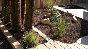 Eine Holzterrasse mit einem rustikalen Zaun, einer Laterne und einem Blumenbeet mit Pflanzen und Steinen.