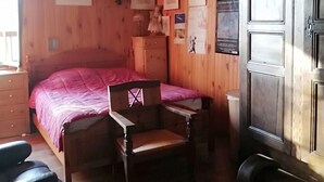 A wooden room with a bed, a chair, a desk, and a wardrobe.