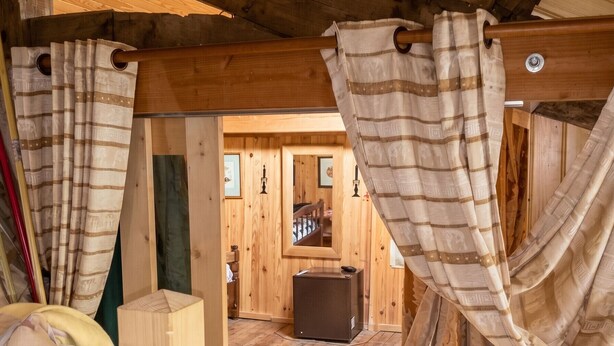 A wooden interior with a bed, curtains, and a wooden cabinet.