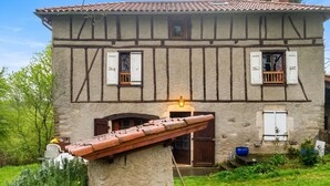 A traditional half-timbered house with a sloped roof, a stone foundation, and a small balcony.