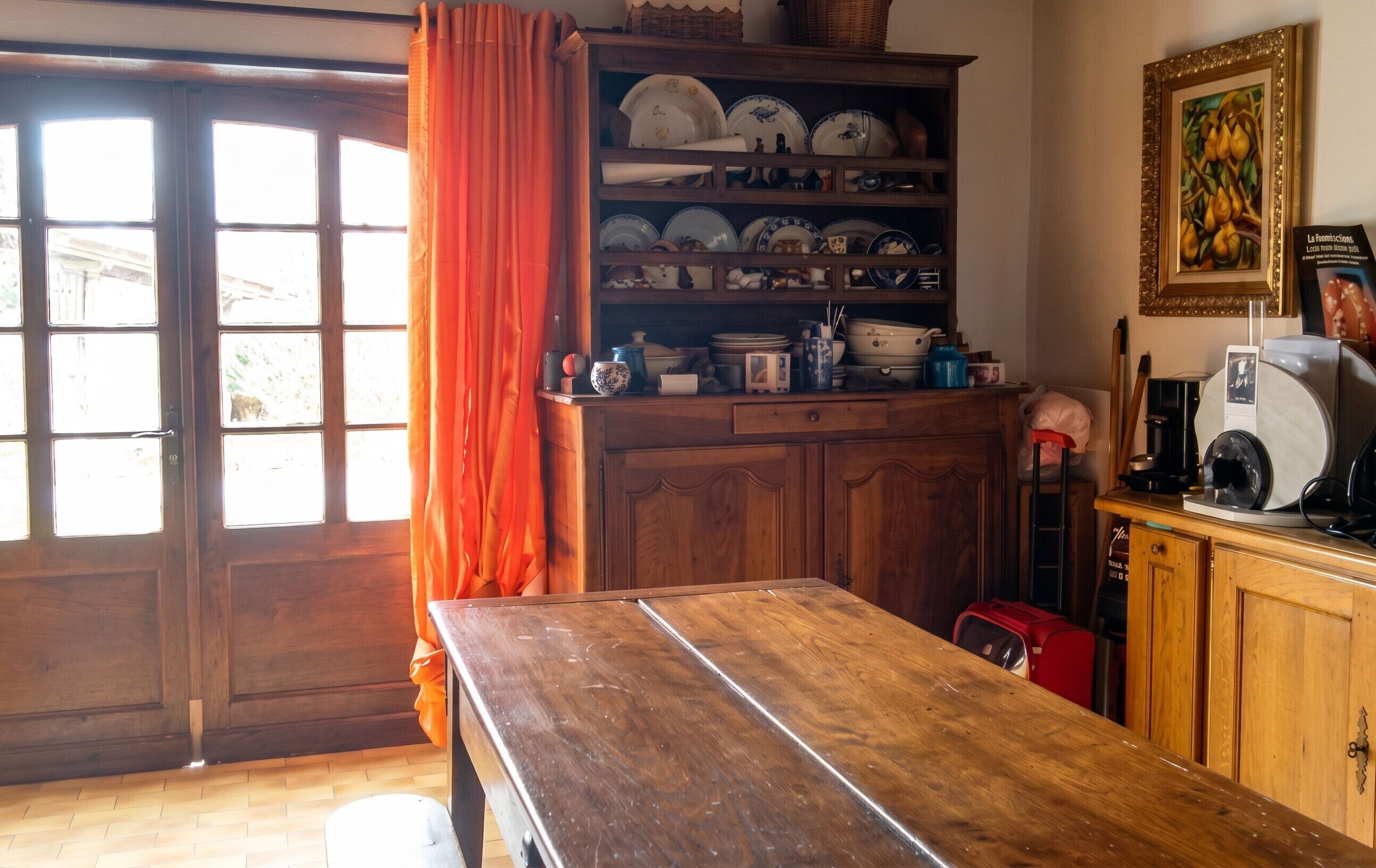A wooden table in a room with a window, a cabinet with dishes, and a vintage radio.