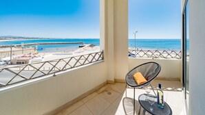 Een balkon met uitzicht op het strand en de zee, een stoel, een tafel met fles en glas, en een betegelde vloer.