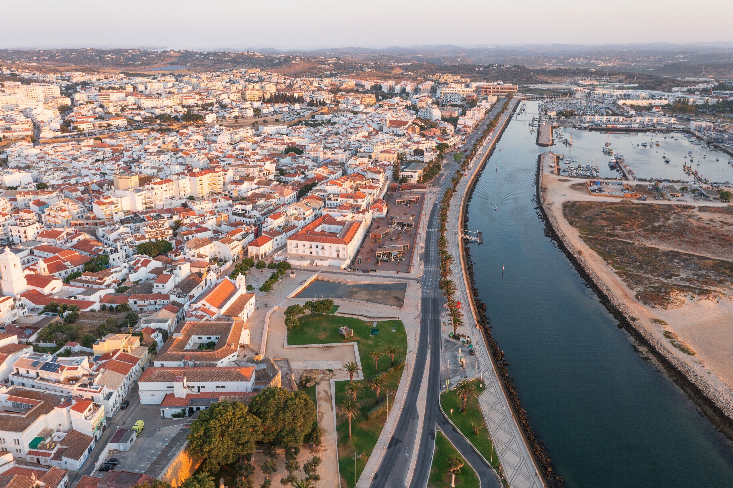 An aerial view of a coastal city with a prominent river, dense urban area, and a marina.