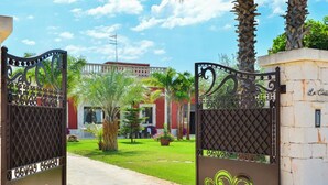 A gated entrance to a property with a well-maintained lawn, palm trees, and a building with a red facade.
