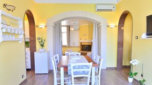 A dining area with a long table, white chairs, and a kitchen in the background.