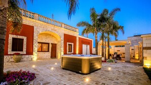 A courtyard with a hot tub, stone walls, and palm trees.