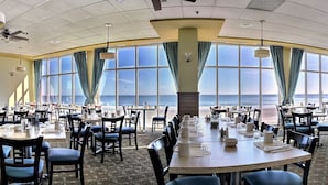 A large dining area with tables and chairs, large windows with curtains, and ceiling fans. - Gorgeous Direct Oceanfront King Suite + Official On-Site Rental Privileges (Myrtle Beach)