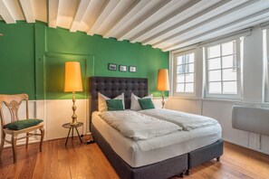 A bedroom with a large bed, two bedside lamps, a green accent wall, and a window with blinds. - Privatzimmer in bester Altstadtlage (Tuebingen)