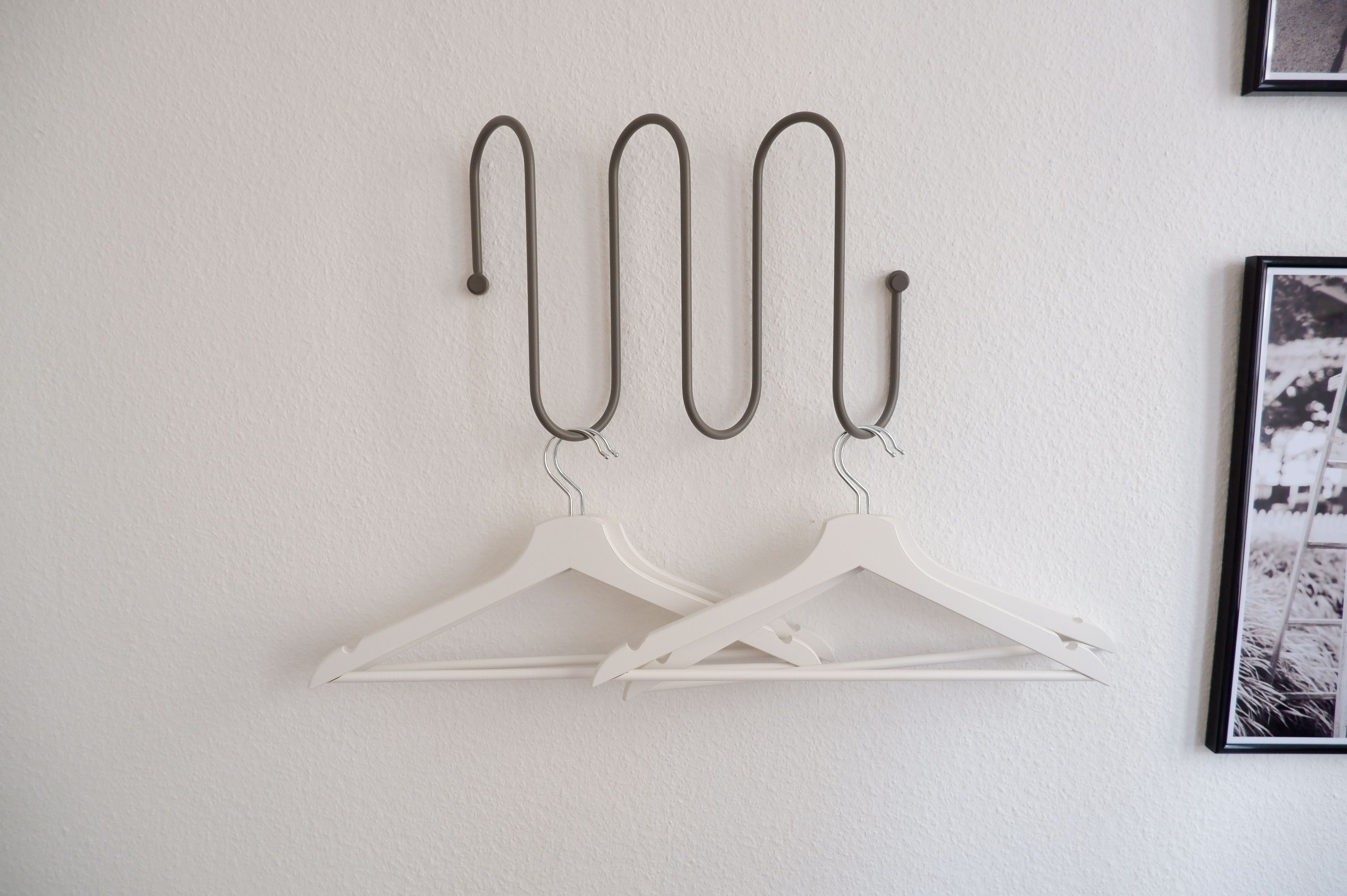 A wall-mounted coat rack with four metal hooks and two white plastic hangers.