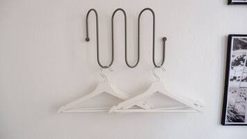 A wall-mounted coat rack with four metal hooks and two white plastic hangers.