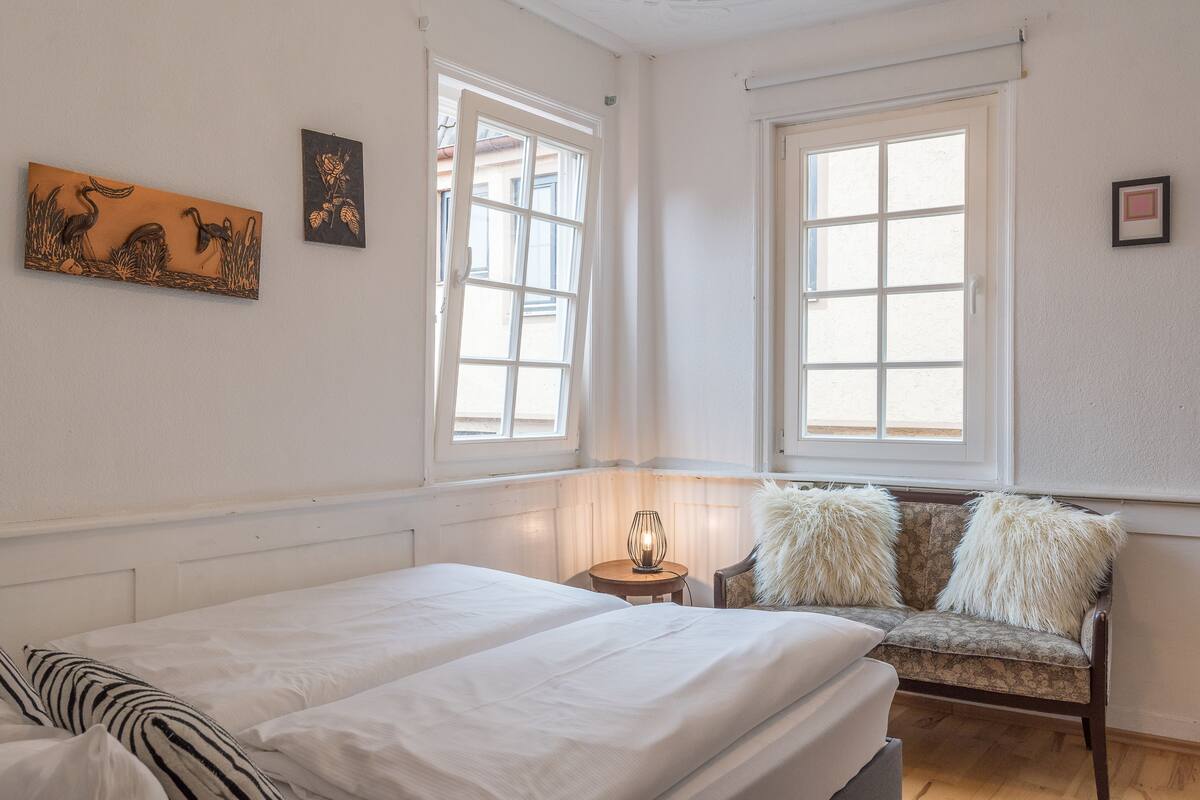 Quarto com duas camas, um sofá, uma luminária e obras de arte nas paredes.