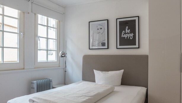 A bedroom with a bed, a radiator, a window, and two framed pictures on the wall. - Privatzimmer in bester Altstadtlage (Tuebingen)