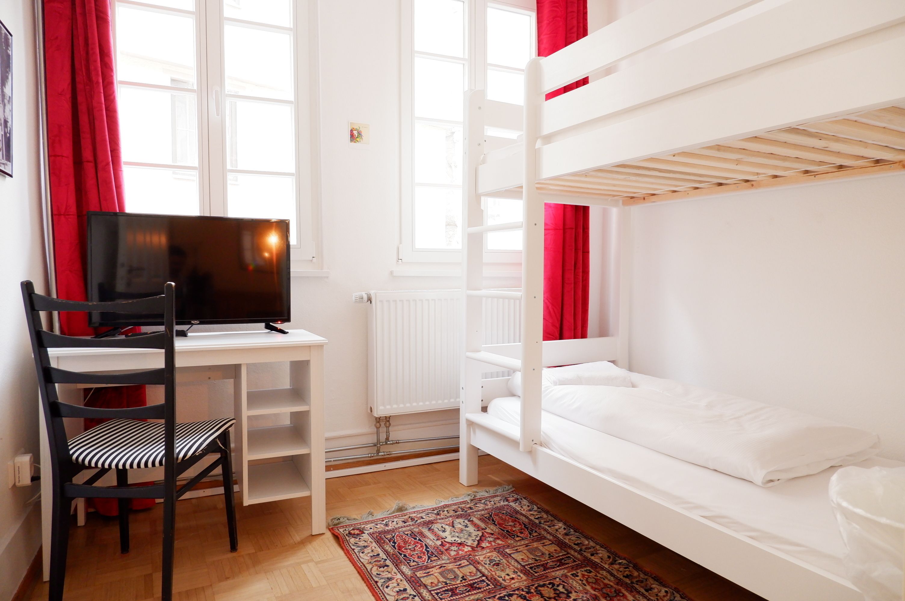 A room with a bunk bed, a desk with a computer, a chair, and a patterned rug.