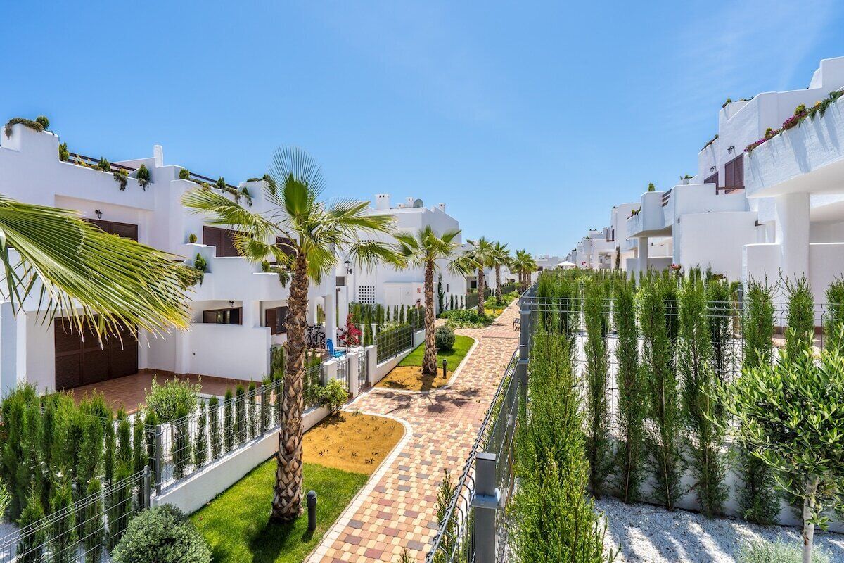 A residential area with white buildings, palm trees, and a paved walkway.
