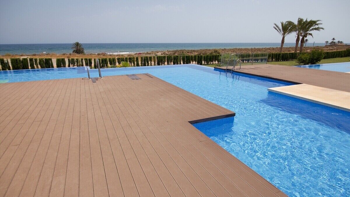 Une piscine avec une terrasse en bois et vue sur la plage.