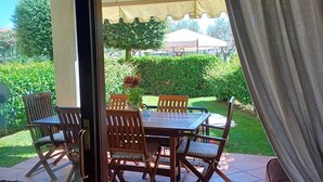 Eine Terrasss mit Tisch und Stühlen, einem hängenden Laternen und Blick auf einen Garten sowie Gebäude im Hintergrund.