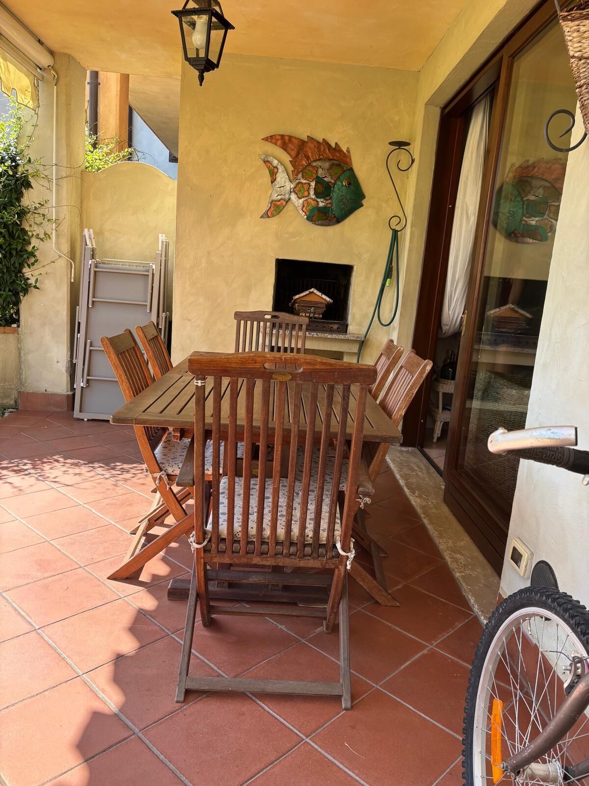 Un patio con una mesa y sillas de madera, una lámpara fijada a la pared y una chimenea.