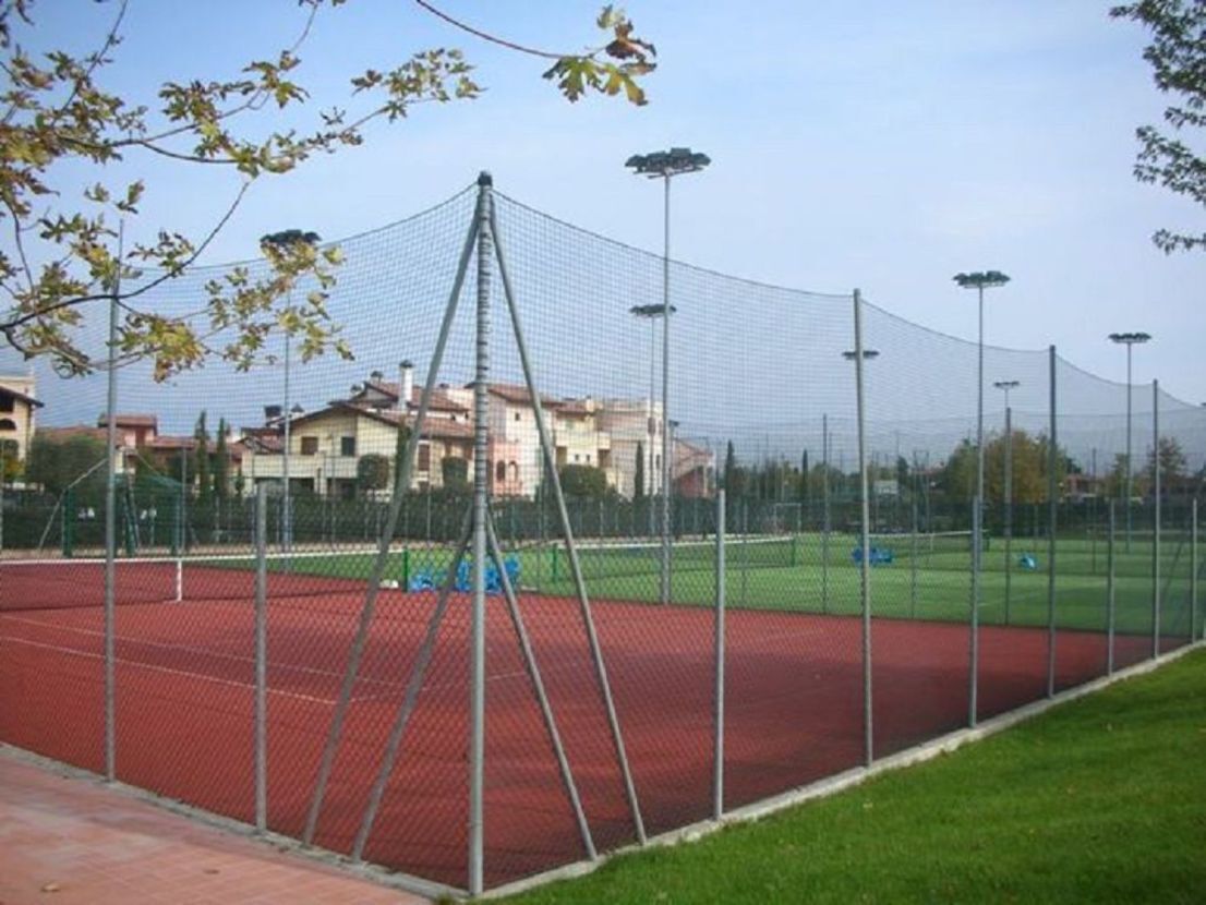 A sports field with a running track and a netted area, surrounded by a fence and street lamps.