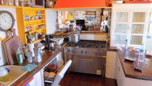 Een keuken met een fornuis, planken met potten, een klok en een rode, driehoekige decoratie erboven.