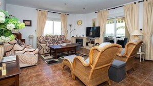 Ein geräumiges Wohnzimmer mit einer Couch, zwei Sesseln, einem Couchtisch und einem Fernseher.