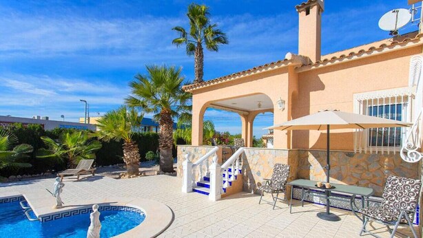 Un área de piscina con terraza de piedra, sillas de descanso y una escalera que lleva a un patio cubierto con mobiliario exterior.