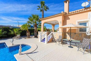 A pool area with a stone-tiled deck, lounge chairs, and a staircase leading to a covered patio area with outdoor seating.